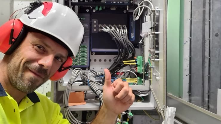 Technicien portant un casque de sécurité faisant un pouce levé devant une armoire électrique ouverte